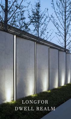 a wall that has lights on it next to some bushes and trees in front of it