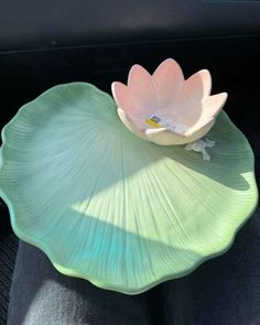 a pink flower sitting on top of a green leafy plate in the back seat of a car