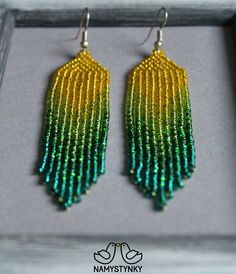 two pairs of beaded earrings with green and yellow fringes on them in a box