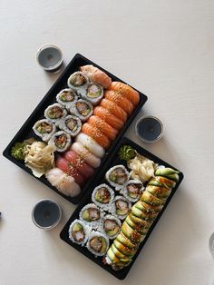 two trays filled with different types of sushi on top of a white table