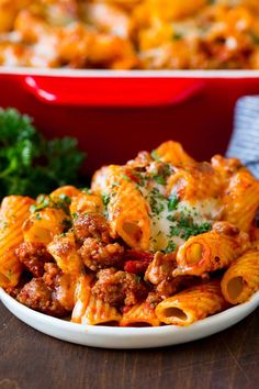 a white bowl filled with pasta and meat next to a red casserole dish