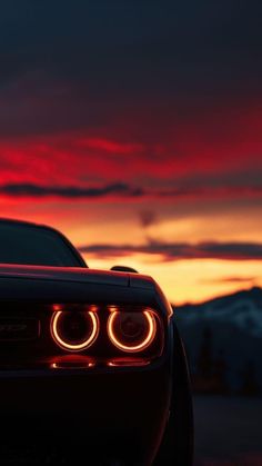 the tail lights of a sports car in front of a red sky with clouds at sunset