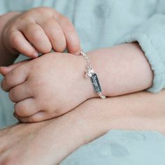 a small child's hand holding onto a bracelet with a cross charm on it