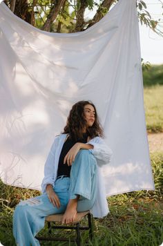 a woman sitting on a chair in front of a white sheet hanging from a tree