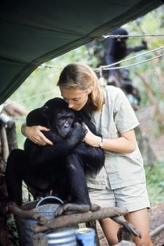 a woman holding a black monkey in her arms while standing next to a metal bucket