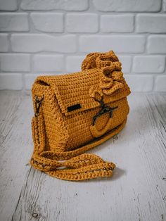 a crocheted yellow purse sitting on top of a white wooden table next to a brick wall