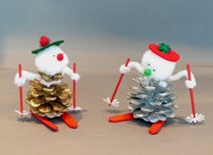 two snowmen on skis are standing next to each other with pine cones in front of them