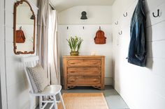 a room with a chair, mirror and coat rack on the wall next to it