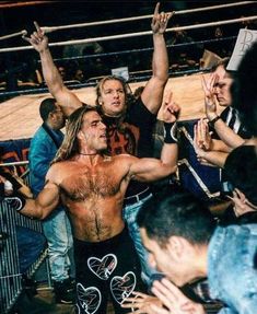 a man standing in the middle of a wrestling ring surrounded by people holding their hands up