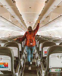 a woman in an orange jacket is walking down the aisle of an airplane with her arms outstretched