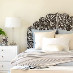 a bed with white pillows and gray headboard in a bedroom next to a night stand