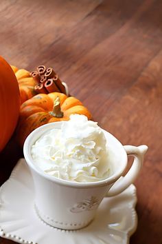 a cup of whipped cream sitting on top of a white saucer next to pumpkins