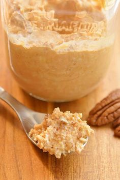 a spoon full of oatmeal sitting on top of a wooden table next to pecans