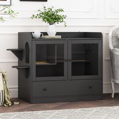 a black cabinet with glass doors and shelves in front of a white chair next to a potted plant