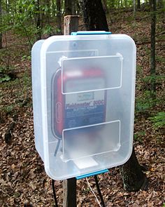 a plastic box with an electronic device in it sitting on top of a wooden post