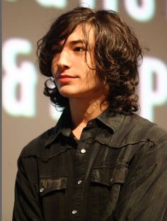 a young man with long hair standing in front of a screen and looking off to the side