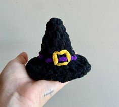 a hand holding a small black crocheted witch's hat with a yellow c on it