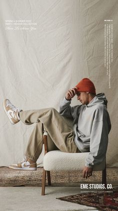 a man sitting on top of a white chair in front of a white wall and wearing an orange hat