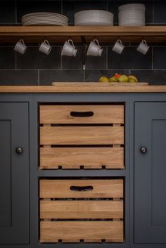 two wooden drawers in the middle of a kitchen with cups on top of them and coffee mugs above