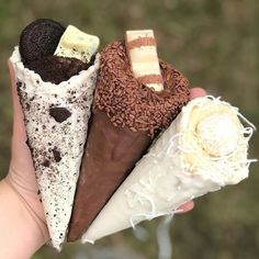 four different types of ice cream cones in someone's hand with chocolate, marshmallows, and oreo