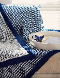 a blue and white blanket sitting on top of a couch next to a tray with a cup