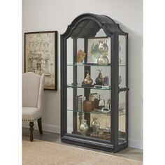 a black display case with glass doors and shelves in the corner next to a chair