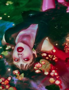 a woman floating in the water with flowers around her neck and eyes painted red on her face