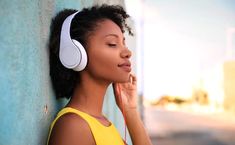 a woman leaning against a wall with headphones on her ears, listening to music