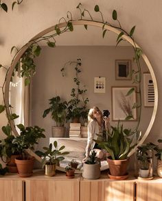 a woman taking a selfie in front of a mirror surrounded by potted plants