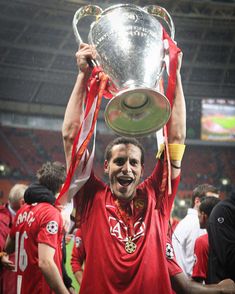 a man holding up a silver trophy in front of his head and other people around him