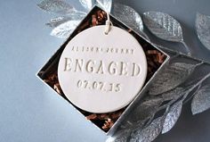 an engaged ornament in a gift box with silver foil leaves on the side