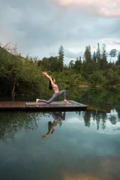 a woman doing yoga on a dock in front of a body of water and trees