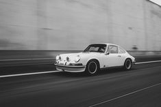 black and white photograph of an old porsche on the road in front of a concrete wall