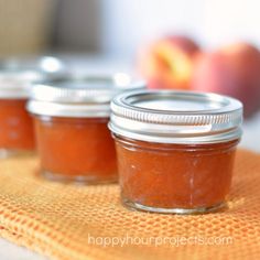 three jars filled with jam sitting on top of a yellow towel next to an apple