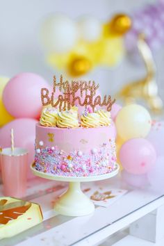 a birthday cake sitting on top of a table with balloons and confetti around it