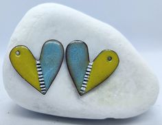 two yellow and blue heart shaped earrings sitting on top of a white rock