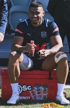 a man sitting on top of a red cooler filled with cans of soda and orange peels