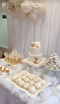 a table topped with lots of cupcakes next to a cake covered in white frosting