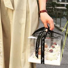 a person is holding a clear box with cupcakes in it on the street