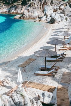 beach chairs and umbrellas are lined up on the sand by the water's edge