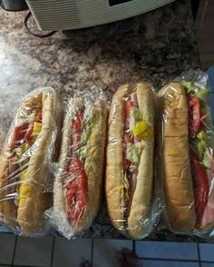 three hotdogs wrapped in plastic sitting on top of a counter next to a microwave