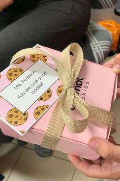 a person holding a pink box with a brown ribbon on it that says, i love you more than cookies