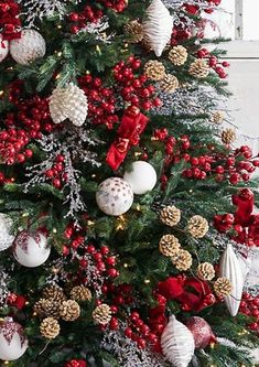 a decorated christmas tree with red and white balls, pine cones, berries and bows