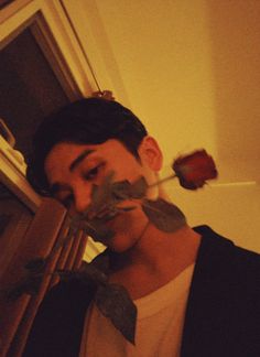 a man with fake leaves on his face and nose is holding a rose in front of him