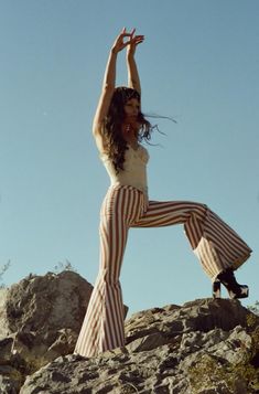 a woman standing on top of a large rock with her arms up in the air