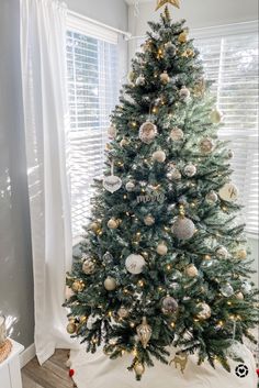 a decorated christmas tree in a living room with white and gold ornaments on the top