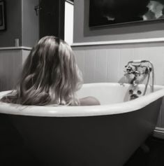 a woman is sitting in the bathtub with her long hair blowing back and looking into the mirror