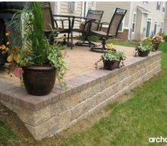 an outdoor patio with chairs and potted plants on the side of it, surrounded by grass