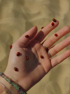 a woman's hand with red and black beads on it, in the sand