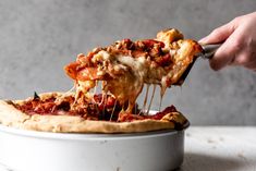 a person taking a slice of deep dish pizza from a white pan on a table